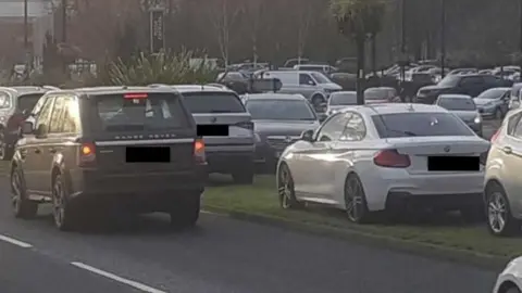Cars parked haphazardly, including on grass verges and in undesignated parking spots at York's Designer Outlet.