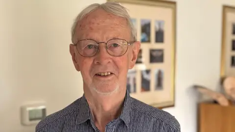 A close up head and shoulders image of Tim Strugnell. He is wearing glasses and a shirt and smiling while looking into the camera.