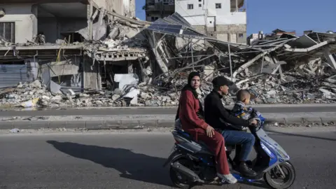  A family riding together on a motorbike passes in front of a building destroyed by Israeli attacks in Tyre, a coastal city in southern Lebanon, has become one of the focal points of intense Israeli air strikes and clashes with Hezbollah since March 2026 on March 17, 2026. 