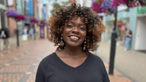 Nyree Hale smiling at the camera wearing a black v-neck t-shirt with shoulder length curly hair