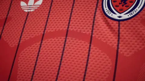 Scottish FA The salmon pink Scotland away shirt with dark purple pinstripes. The image focuses on the pinstripes.
