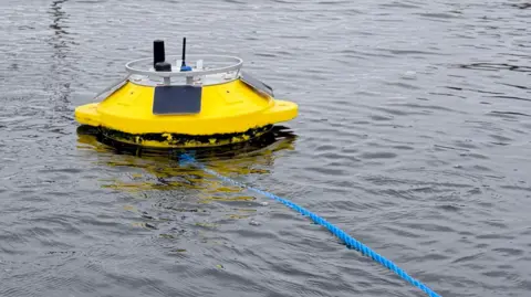 A yellow spaceship-like device floating in water. There is a blue rope attached to it.