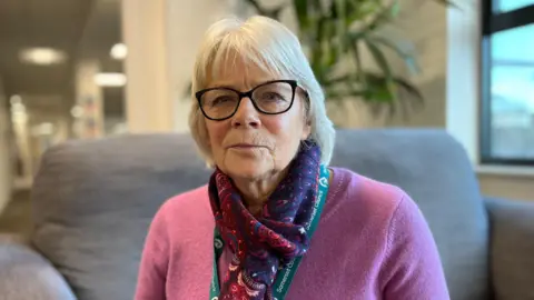 Liz Leyshon sitting on a sofa starring at the camera.