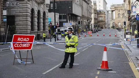 PA Media A lone police officer in high visibility uniform guards the scene of the incident in central Liverpool
