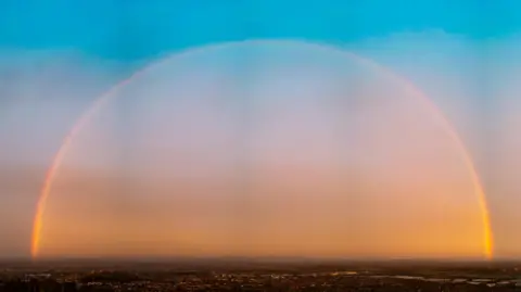 Phil Harrison/Weather Watchers A rainbow can be seen in the northern sky with blue sky above it and a hazy sunrise below