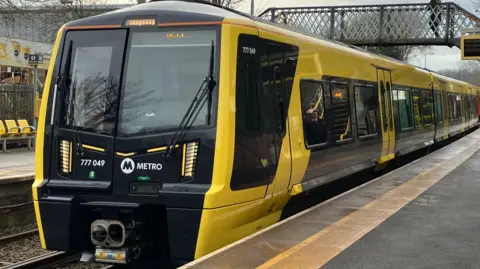 The Merseyrail train is black and yellow, and has stopped at a platform.