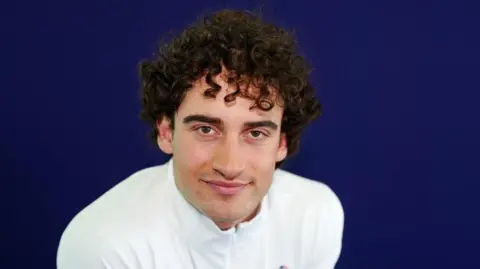 PA Media Mateo Jeannesson during a kitting out session, in front of a blue screen, wearing a white top, he has short dark curly hair. He is looking straight at the camera. 