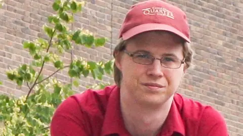 Supplied A slightly grainy picture of Jon wearing a red polo shirt and cap, as well as glasses.