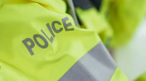 A close‑up of a high‑visibility yellow jacket with the word “POLICE” printed in bold reflective letters across the back.