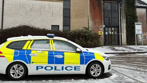 A police car sits outside Kirkwall Police Station, covered in snow. 