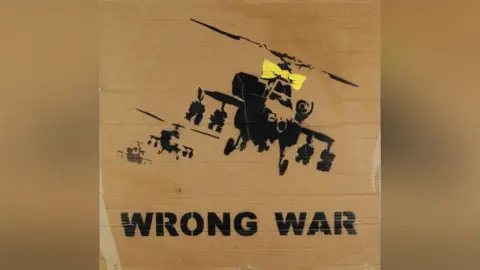 Eastbourne Auctions A placard showing three helicopters, one with a yellow bow on it, with writing reading "Wrong War"