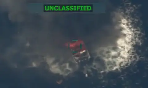 Pete Hegseth X account A still from a surveillance video showing a boat in the ocean with smoke and fire coming off of it. It says unclassified in neon green all-capped letters.