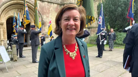 First Minister Eluned Morgan, who has short brown hair and is wearing a green jacket, red top and a gold chain around her neck