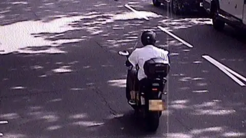 PA A moped with a rider in a white shirt wearing a helmet. The marking on the road can be seen to the right of him. 