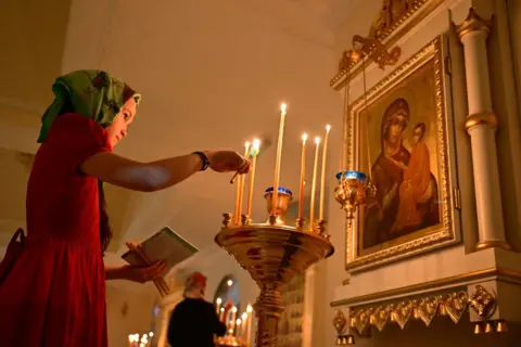 Getty Images Seorang jamaah menyalakan lilin saat perayaan Malam Natal Ortodoks di Gereja Ortodoks Rusia di emirat Teluk Sharjah pada 6 Januari 2025.