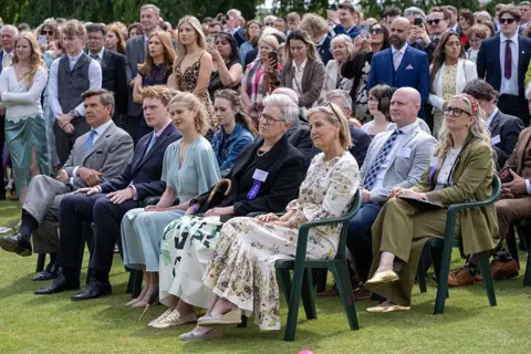 Getty Images A group of people including Sophie, Duchess of Edinburgh, and Lady Louise Mountbatten-Windsor sit with other VIPs in the gardens of Holyroodhouse. There are many young people in the background.