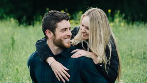 Harper family Andrew and Lissie Harper smiling at each other in a grassy field.