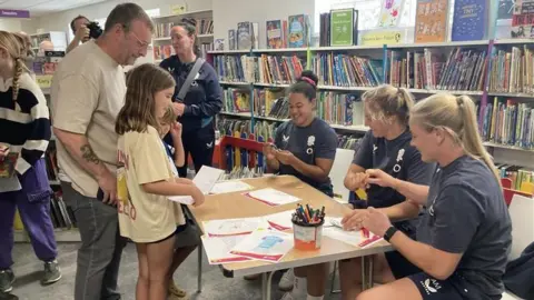 James Burridge/BBC England rugby players meeting a young girl and a man at a library