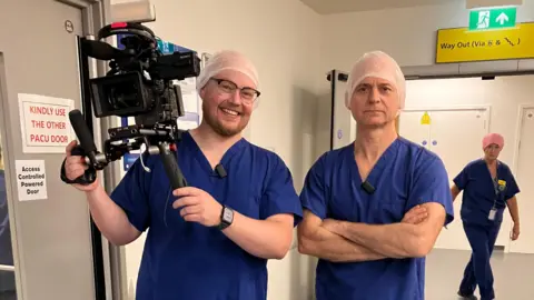 Camera Operator Jack Champion and Health Correspondent Alastair Fee wearing blue scrubs at Heatherwood Hospital.