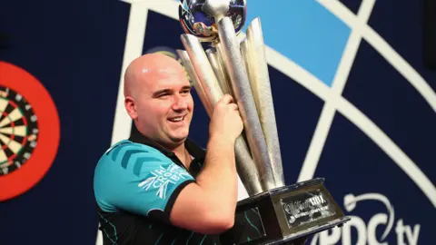 Rob Cross holding the world darts championship trophy.