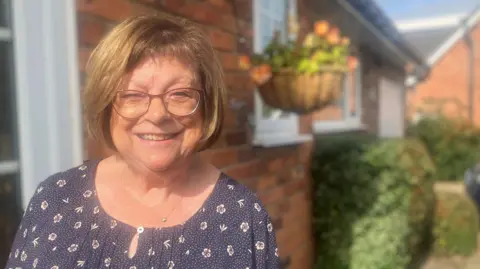 Photograph of Janet Stockton from Cheshire. She is pictured outside her home in the village of Adlington. 