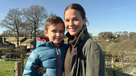 Freddie and his mum, Lauren, stand in the sunshine in fields near their home in Huddersfield