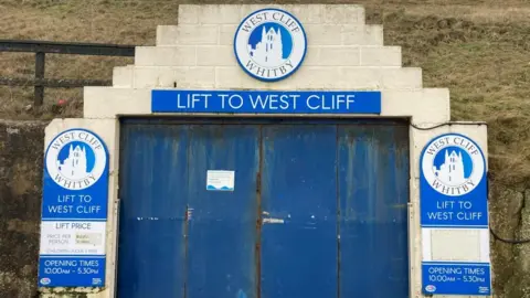 Blue doors which are closed. Signs read "Lift to West Cliff".
