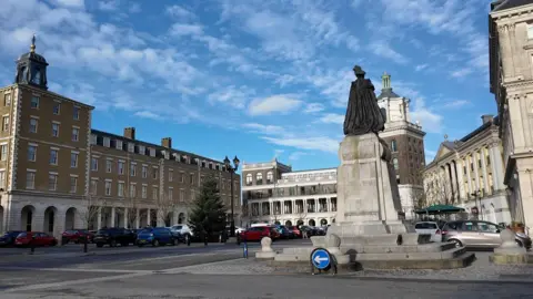 A street in Poundbury with a bronze statue and a semi-circle of buildings.
