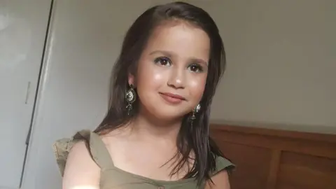 SURREY POLICE Sara Sharif, wearing make-up and a beige dress, looks into the camera.