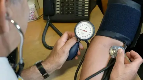 PA Media A man takes blood pressure using a blood pressure monitor 