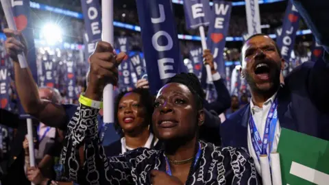 Reuters: Supporters of Joe Biden hold up signs with his name during a speech at the Democratic Party Convention