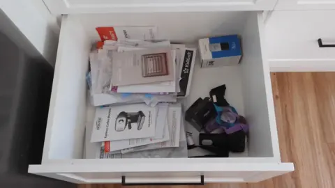 Supreme Court of Victoria White kitchen drawer pulled out to display a two piles of instruction manuals on the left (one at the top and one at the bottom. At the top of the pile on the top left of the drawer, is the instruction manual for the dehydrator.