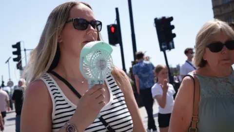A woman cools her face with a hand-held electric fan