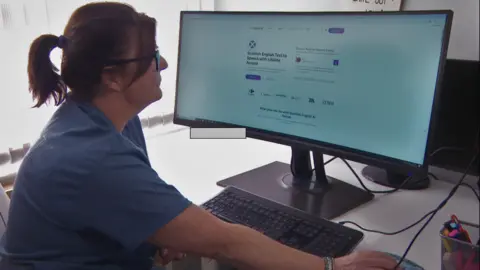 Gayanne is sat at her desk, staring at a computer screen which has the ReadSpeaker website opened. It says "Scottish English Text to Speech with Lifelike Accent".