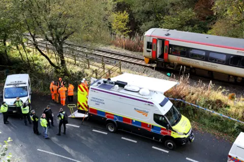 Members of the police and Network Rail stood on the side of a railway track with a broken down train behind