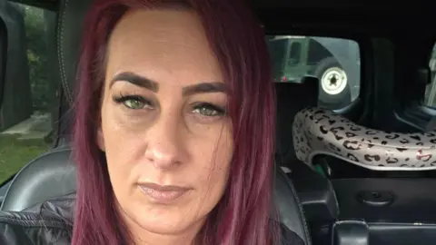 Josephine Quinton Josephine Quinton with long red-coloured hair, looking at the camera and wearing a black leather jacket. She is sitting on a black leather chair.