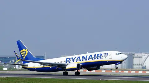 Ryanair plane taking off from a runway. The plane is white, blue, yellow.