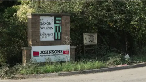 A general view of the exterior sign to Saxon Pit. A sign says "Saxon Works Entrance", with "Johnson Aggregates and Recycling" below it.