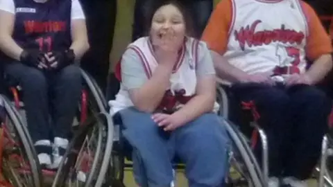 PA Kaylea in a wheelchair with a big smile and a hand over her mouth.