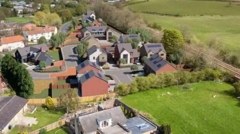 LDRS Artist's impression of a development of new homes, showing some green fields around the outside and a railway line running next to it.