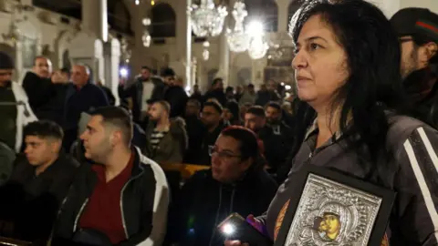 Getty Images A woman holds a framed artwork of the Virgin Mary and baby Jesus as she stands sombrely in a crowd