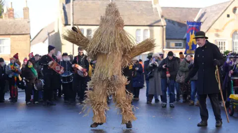 PA Media A man dressed as a straw animal in front of a crowd. 