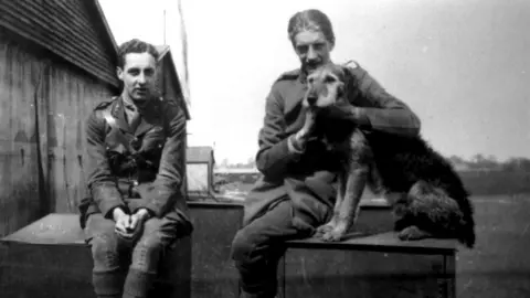 Stow Maries A black and white image of two airmen sitting on crates at Stow Maries with a dog.