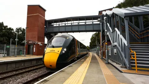 Great Western Railway A yellow and black train approaching Ashley Down Station, with steps and a footbridge in view.