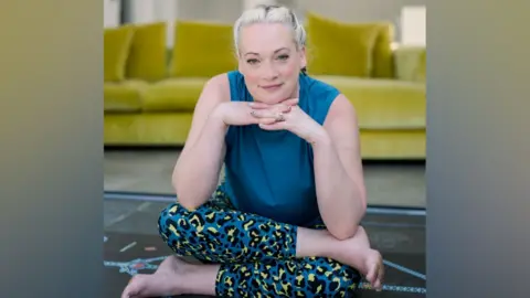 Contributed A woman sits on the floor with her head resting atop of her hands. She is sitting in a yoga pose with her legs crossed. She wears blue, yellow and black leggings in an animal print pattern with a blue top. There is a lime green sofa behind her.