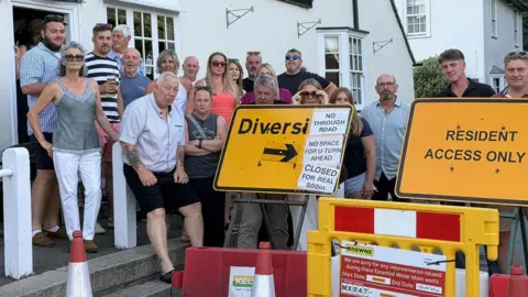 Supplied Yellow signs for roadworks outside a pub with several people standing behind them.
