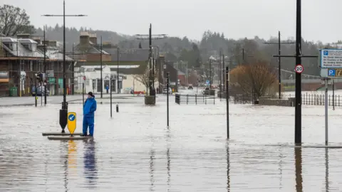 The Whitesands car park and road under flood water with a man wearing blue waterproofs standing on a traffic island