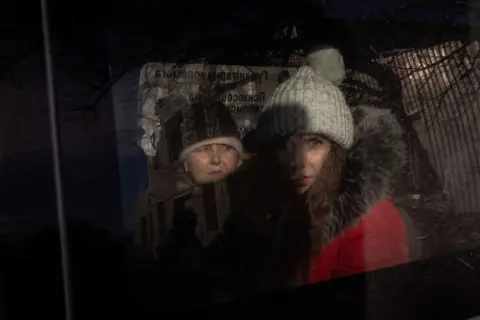 Roman Pilipey/AFP Two women, some  wearing hats and lukewarm  coats, look   retired  from the model   of a car