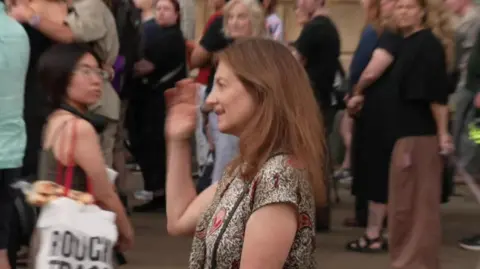 Deborah Prentice - the vice-chancellor of the University of Cambridge - attending a vigil in the city centre. Crowds of people are looking towards her.