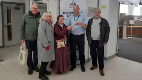 supplied A small group of people handing over a letter to man with a lanyard in front of a council banner